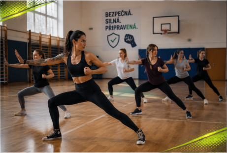 Trenérka vede workshop osobní bezpečnosti ve&nbsp;školní tělocvičně, ženy ve&nbsp;sportovním oblečení napodobují obranné a&nbsp;pohybové cviky.